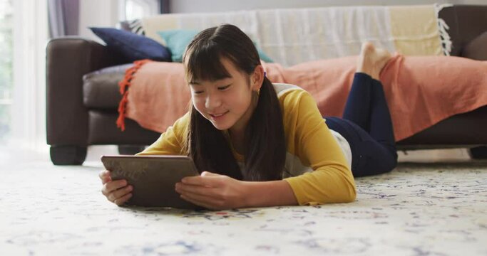 Asian girl smiling and using tablet lying on floor at home