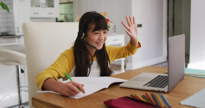 Happy asian girl at home, sitting at desk smiling during online school lesson using laptop