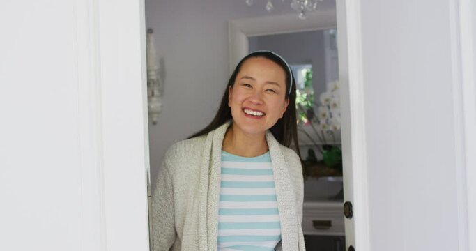 Happy asian woman opening front door, smiling and greeting visitor to home