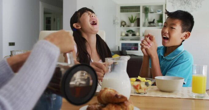 Happy asian brother and sister in kitchen having breakfast and laughing with parents