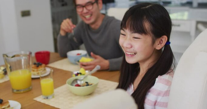 Happy asian father in kitchen eating breakfast with laughing son and daughter