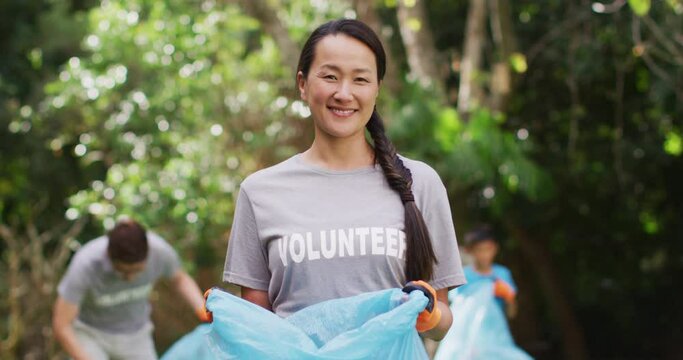 Smiling asian woman wearing volunteer t shirt holding refuse sack for collecting plastic waste