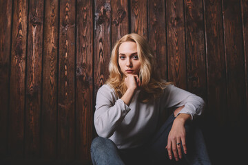 Thoughtful woman near wooden wall touching chin