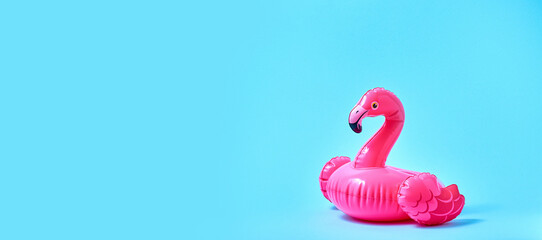 Inflatable pink flamingo pool toy on blue background. Creative minimal concept. Banner