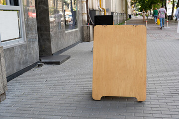 blank wooden advertising board stands on a street. an advertising board for writing a menu or assortment stands on the street near the restaurant, daytime.
