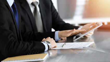 Businessman using tablet computer and work together with his colleague in sunny modern office, close-up. Unknown business people at meeting. Teamwork and partnership concept