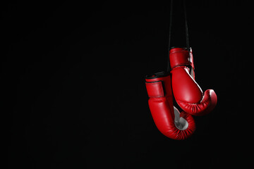 Pair of red boxing gloves hanging on black background, space for text