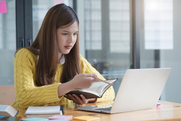 Student studying and writing notes in a notebook at home, making research on laptop and browse internet, watching online webinar, listening audio course, e-learning education concept
