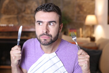 Anxious man holding knife and fork - obrazy, fototapety, plakaty