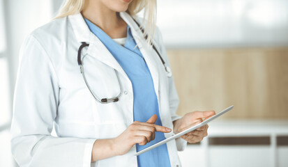 Unknown woman-doctor standing in clinic and using tablet pc, close-up. Data and best service in medicine and healthcare