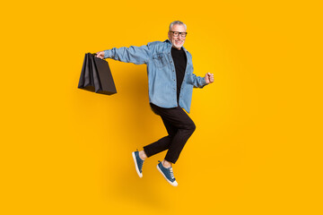 Fototapeta na wymiar Full size profile photo of funky granddad hold bags jump wear jacket pants isolated on yellow color background