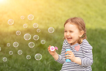 Emotional laughing child girl blowing soup bubbles in sunny summer nature. Fresh green grass...