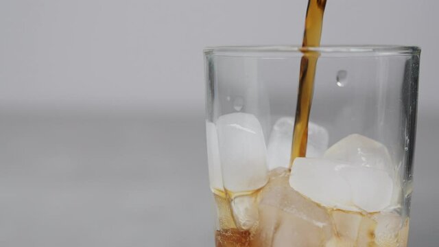 Slow motion 4K. A sweet  cold soft drink is poured into a glass filled with ice cubes. refreshing delicious drink Thirst quenching drink.
