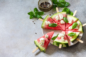 Healthy seasonal dieting and nutrition, summer snack. Watermelon pizza with feta cheese and basil on a gray stone tabletop. Copy space.