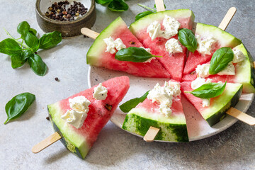 Healthy seasonal dieting and nutrition, summer snack. Watermelon pizza with feta cheese and basil on a gray stone tabletop.