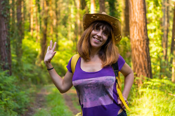 Traveler woman smiling with hat and looking at the forest pines, hiker lifestyle concept, copy and...