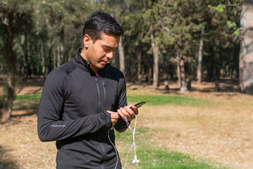 Young Latino man using his cell phone while running through the forest on a morning while listening to music.
