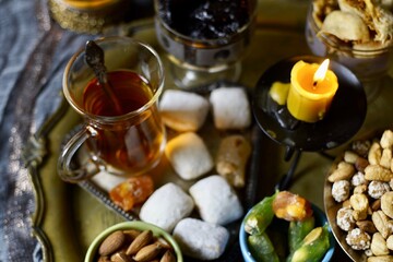 A table with Turkish tea with lale, oriental sweets, rahad delight, a mix of various nuts using copper dishes and bright fabrics.