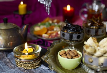 A table with Turkish tea with lale, oriental sweets, rahad delight, a mix of various nuts using copper dishes and bright fabrics.