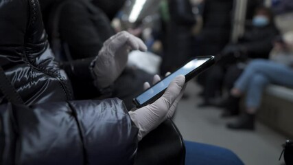 Mature woman in medical mask and protective gloves uses smartphone while traveling in subway car. New life reality concept and precautions for COVID 19 pandemic. Healthy and safety life theme