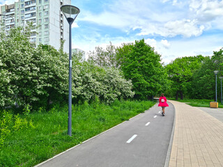 The girl in red rides a scooter along the bike path in the park.