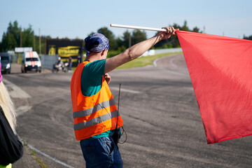 A marshal at a racetrack holds up a red flag to the rider(s).