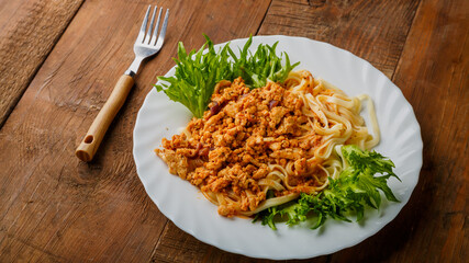 A plate of bolognese pasta decorated with herbs on a wooden table next to a fork.