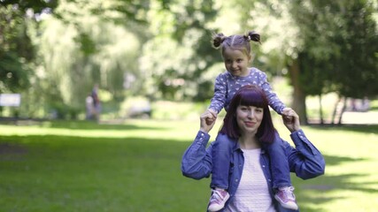 Cute little 3-aged daughter on a piggy back ride with her charming mother, walking in beautiful city summer park. Happy girl and mom laughing and enjoying together during walk in park