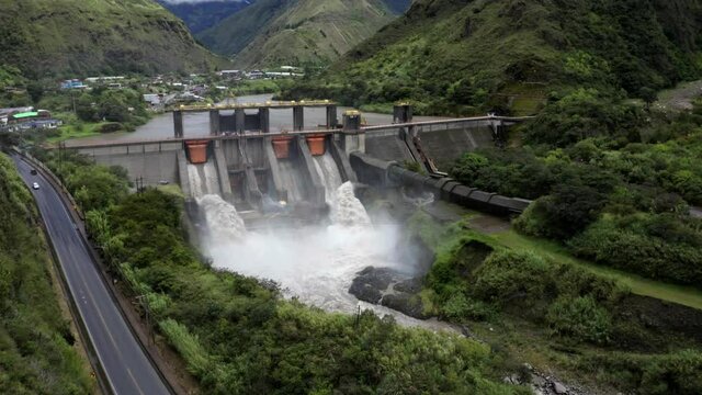 Aerial side view, flying towards a large hydroelectric dam with water rushing through the open gates