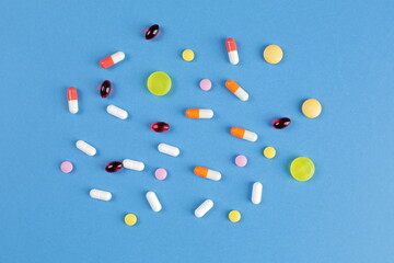 Multicolored medical pills of various shapes on a blue background
