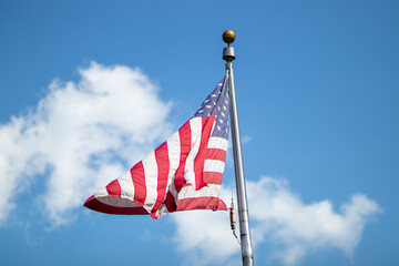 United States flag blowing in window against blue sky with cloud during day in summer