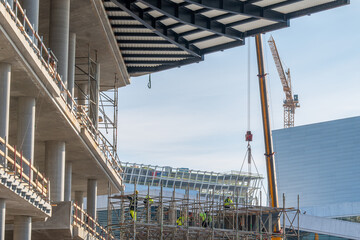 Construction workers on a scaffolding in a large unfinished concrete building with pillars and bare detail