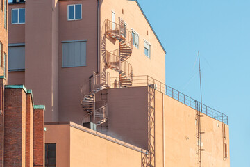 Tall industrial building section with bright colored walls and winding spiral outside staircase against a clear blue sky