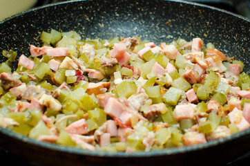Pickled cucumbers and smoked meat are fried in a pan. Cooking at home.