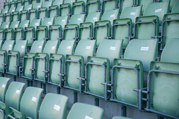 Closeup of empty green folding stadium seats in long rows on grey concrete base with grey metal railings and labels marked athelete