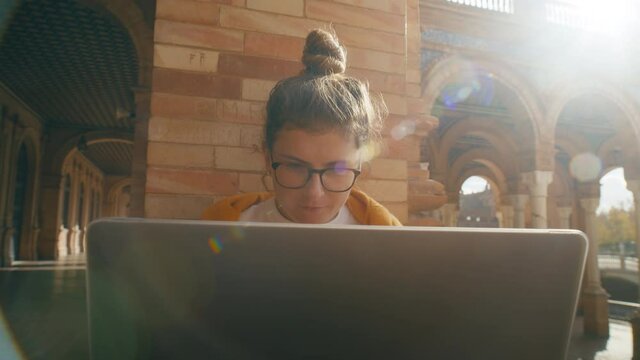 Young student work on laptop at university campus. Red brick old school empty building. Working on phd project or school assignment. Homework for postgraduate education