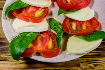 Plate with caprese salad (italian salad with cherry tomatoes, mozzarella cheese and basil leaves) on wooden table