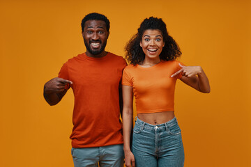 Beautiful young African couple gesturing and smiling while standing against yellow background