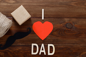 Happy fathers day concept. Black paper mustachewith a gift on table background with the inscription - I love dad.Copy space
