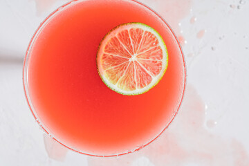 Salt rimmed Paloma cocktail  with tequila and grapefruit juice, lime slice garnish on white table,...