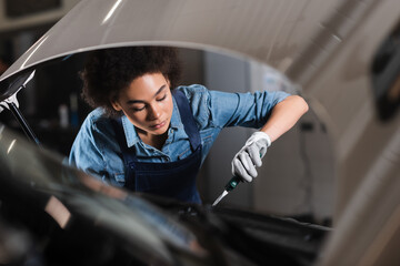 young african american mechanic holding pliers and working with motor of car in garage