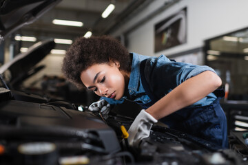 young african american mechanic fixing motor in car with open hood in garage - obrazy, fototapety, plakaty