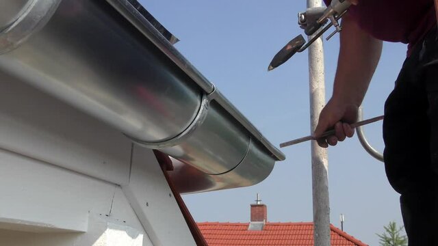 Dachdecker bei Spenglerarbeiten an einer Dachrinne