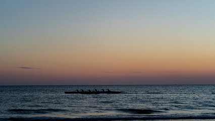 Rowing crew in silhouette on water against pastel sunset sky