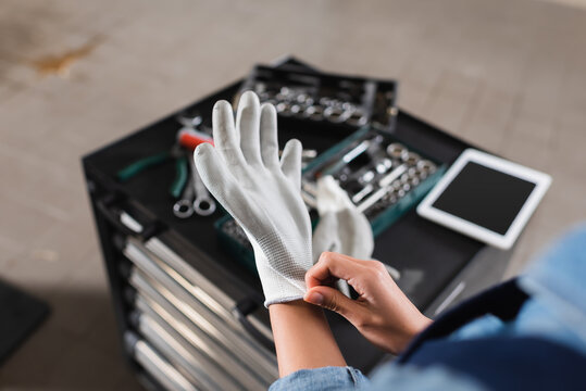 partial view of young mechanic wearing glove on hand near toolbox and digital tablet in garage