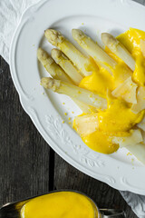 White asparagus with hollandaise sauce, parmesan and lemon zest on white plate on wooden table.