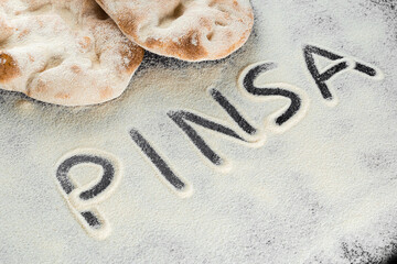 Dough and flour with text pinsa on black background. Pinsa romana and scrocchiarella gourmet italian cuisine. Traditional dish in italy.