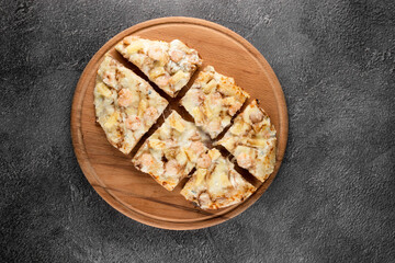 Pinsa romana with shrimps and pineapple on wooden plate on dark background. Seafood scrocchiarella.