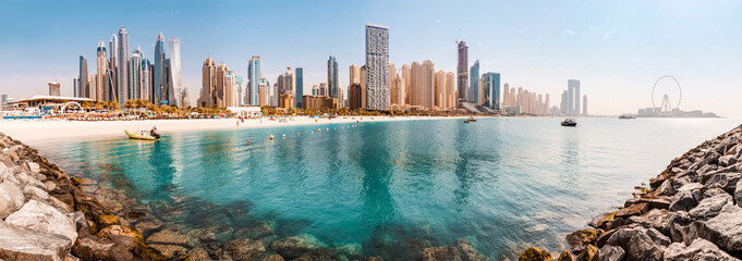 Fototapeta Wide panorama of the Persian Gulf with sandy beach and Bluewaters Island with the worlds famous largest Ferris wheel Dubai Eye and numerous skyscrapers with hotels and residences obraz