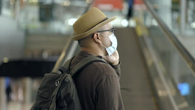 Traveler man wearing mask protect flu coronavirus. Tourist in airport terminal using smartphone standing at escalator. During the pandemic must be social distancing self quarantine.